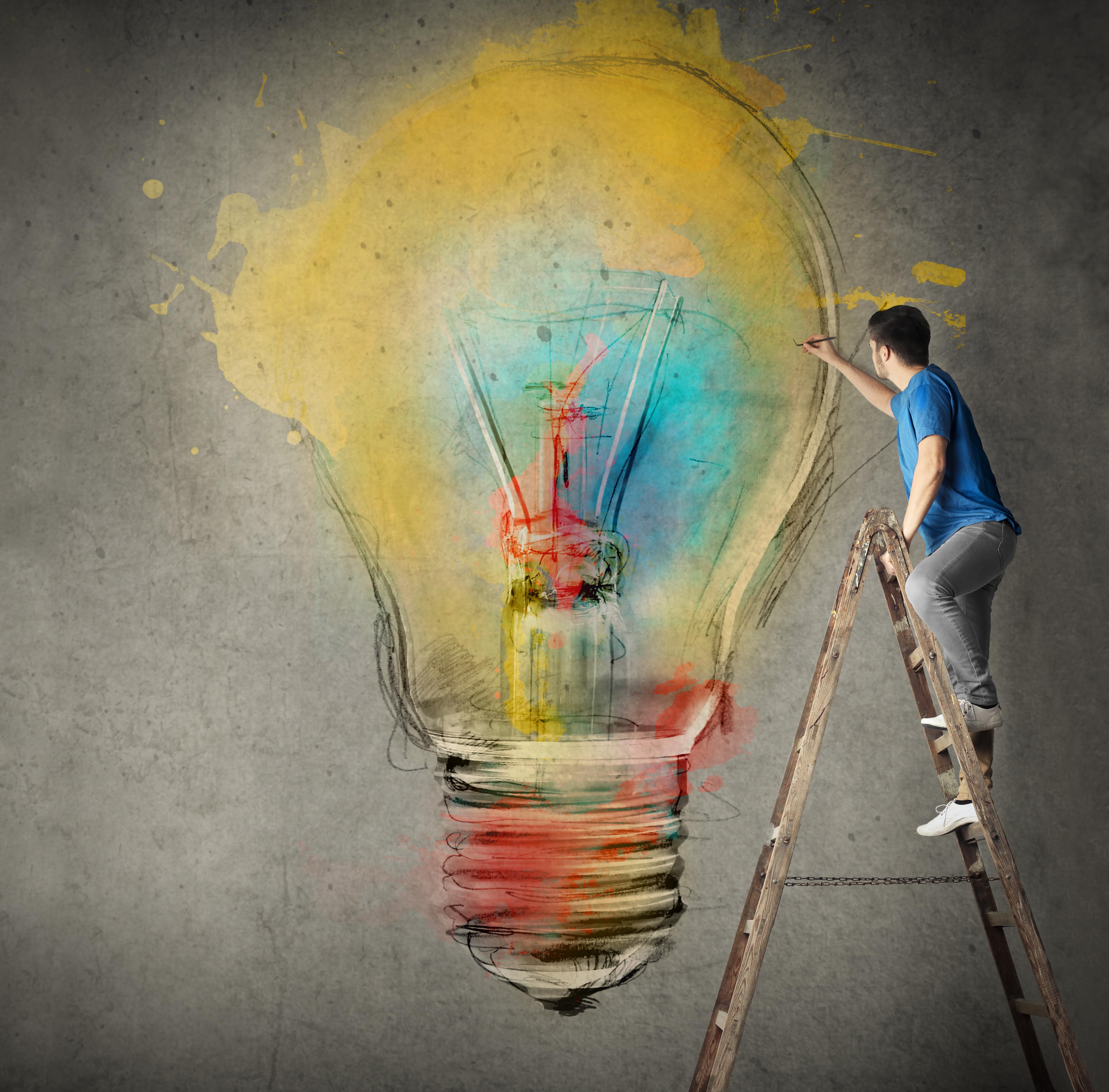 Man on ladder drawing a lightbulb 