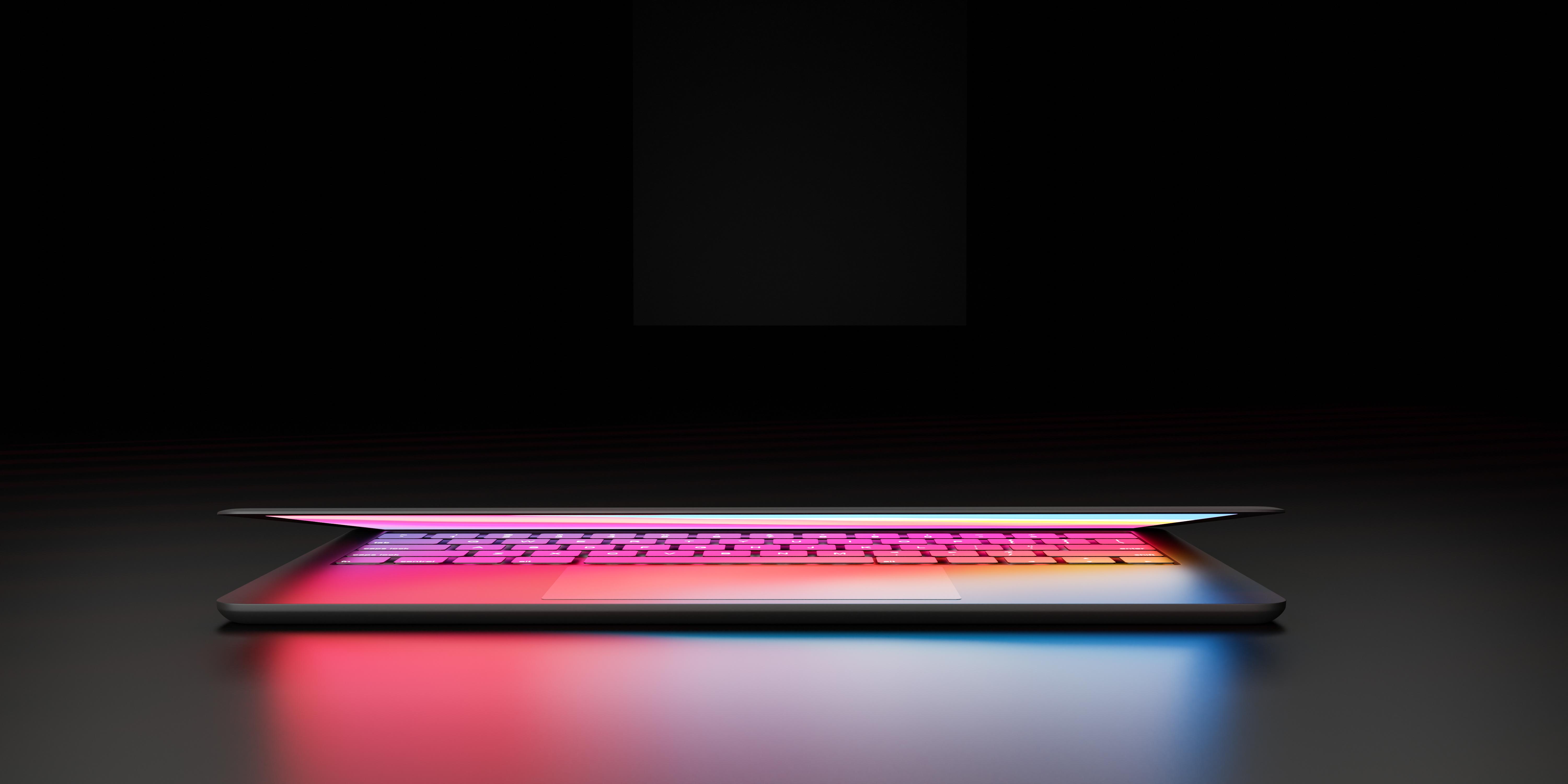 Laptop with backlit pink and yellow ombre colors slightly open with a black background
