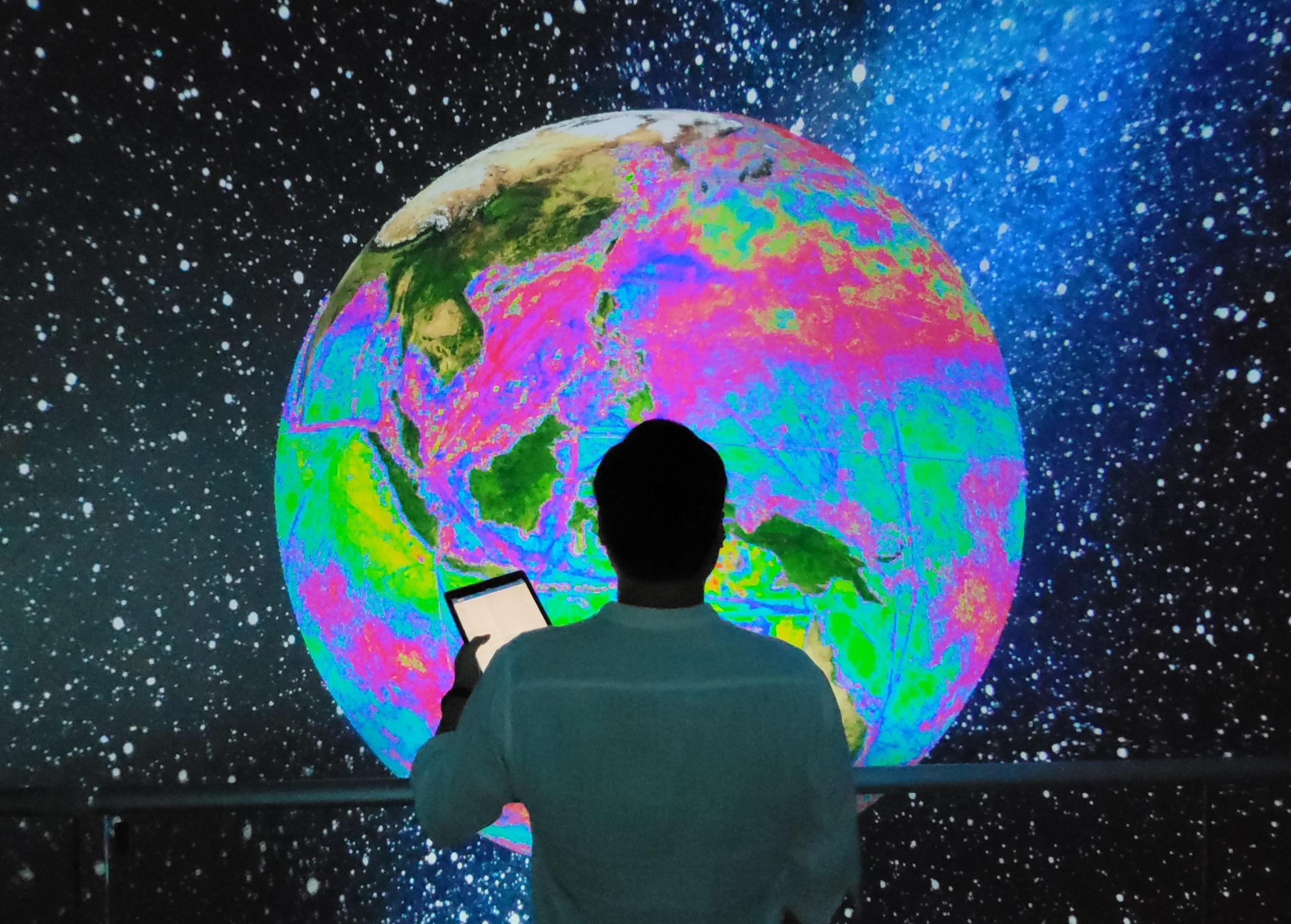 A person standing in front of a digital representation of the earth with bright colors.