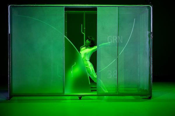 Dancer in white leotard behind a frosted screen in a dance post under green lighting.