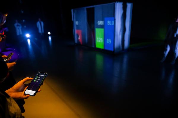 Audience members engaging with a phone application to indicate the next interaction the dancers will have with the small robot.